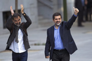 Jordi Cuixart, presidente de la organización de Cataluña Ómnium Cultural, a la izquierda, y Jordi Sánchez, presidente del grupo Asamblea Nacional Catalana, saludan a simpatizantes a su llegada a la Audiencia Nacional en Madrid, España, el lunes 16 de octubre de 2017. (AP Photo/Francisco Seco)