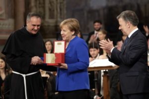 La canciller alemana Angela Merkel, centro, flanqueada por el presidente colombiano Juan Manuel Santos, derecha, y el padre Mauro Gambetti recibe el premio de la paz Lámpara de San Francisco en la Basílica de Asís, Italia, sábado 12 de mayo de 2018. (AP Foto/Alessandra Tarantino)