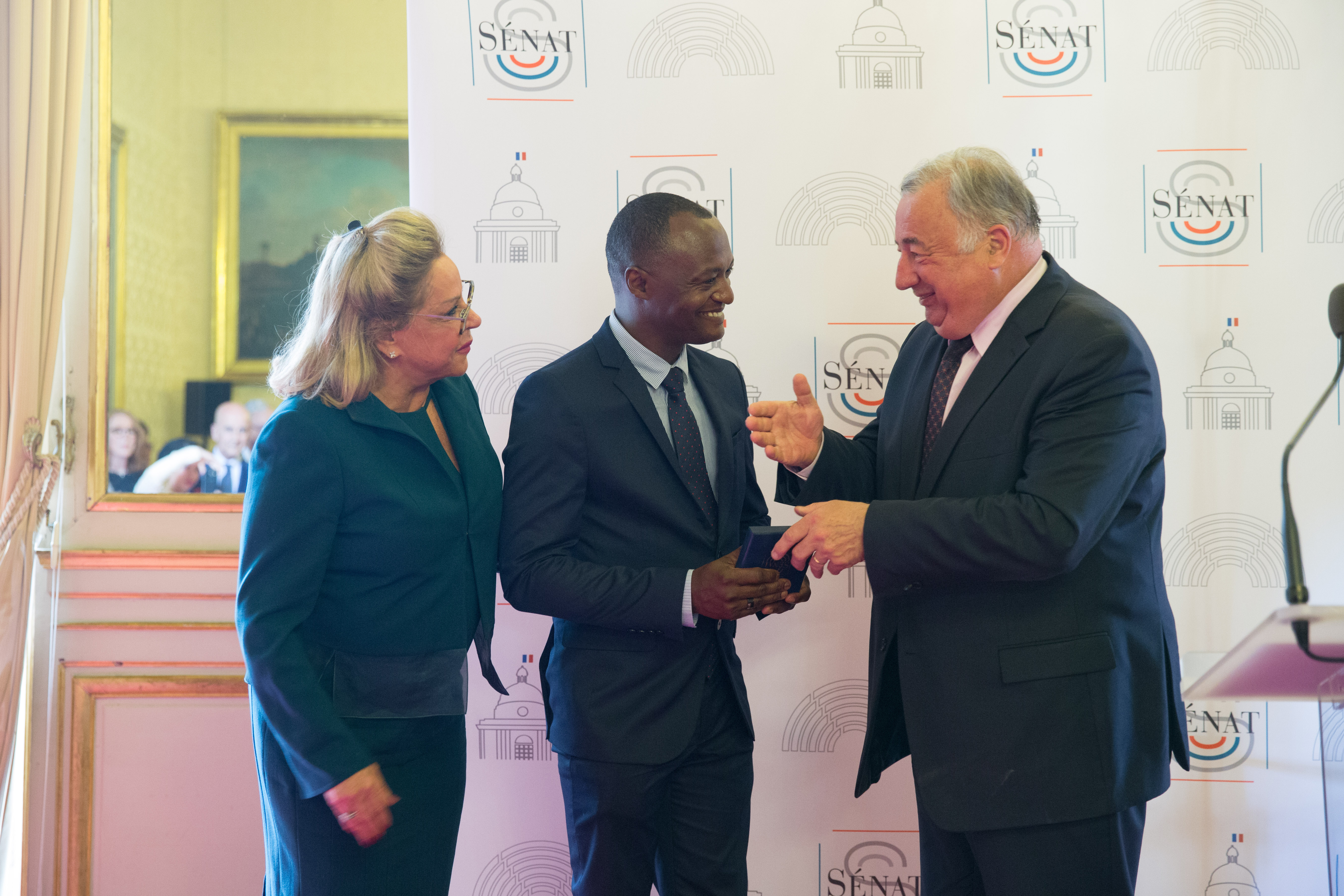 El señor Gómez Campusano acompañado de la embajadora dominicana en Francia, Rosa Hernádez de Grullón recibe de manos de Gérard Larcher, presidente del Senado, la medalla al reconocimiento por sus aportes a la comunidad en la que reside y trayectoria artística en ese país.