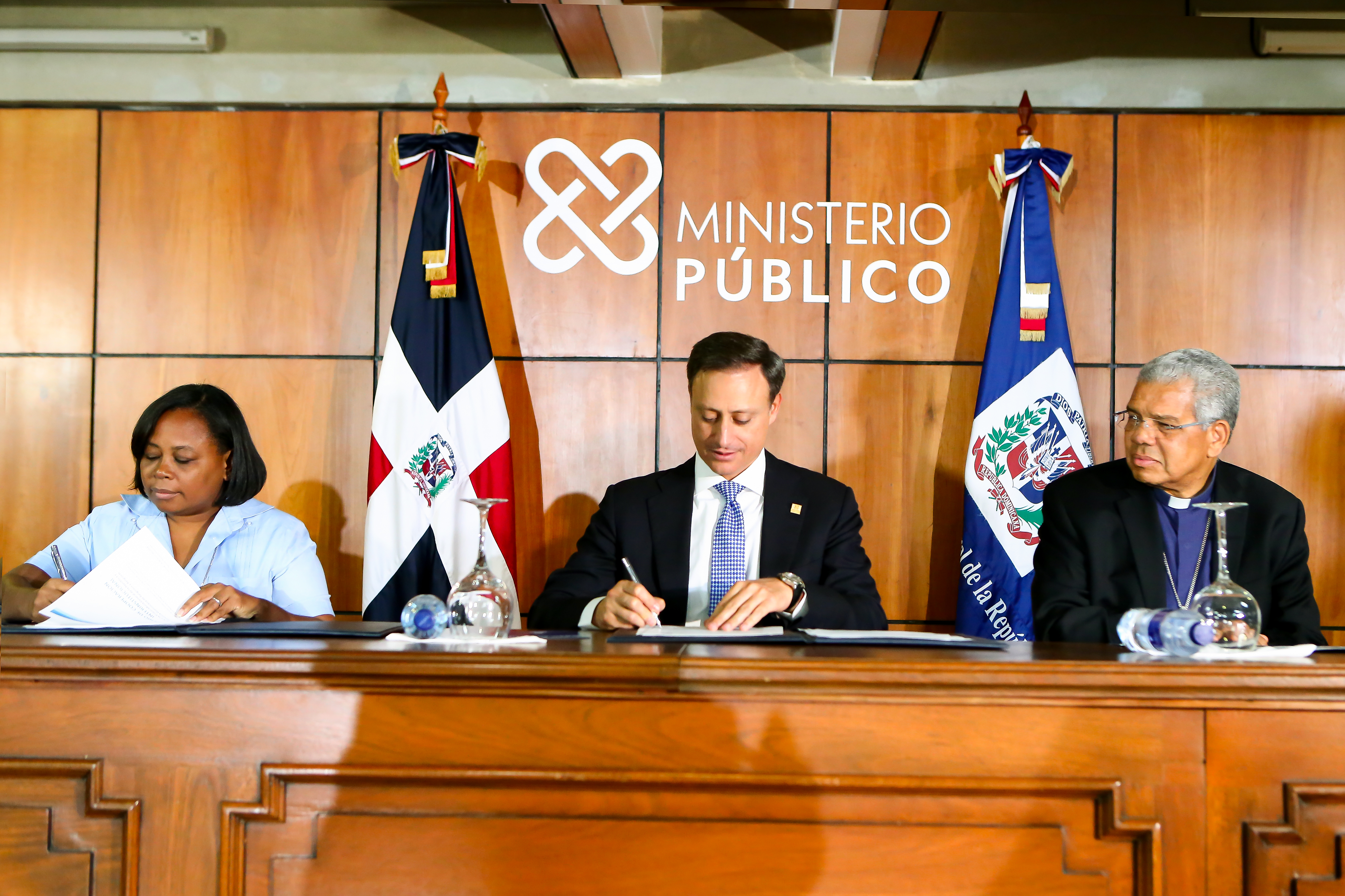 El procurador Jean Rodríguez y la presidenta de CONDOR, Hermana Patria Fernández Céspedes, mientras firman el acuerdo de cooperación interinstitucional Para proteger víctimas de trata de blancas. Observa, monseñor Francisco Osoria Acosta.