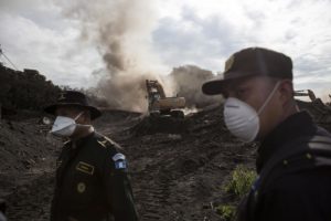 Esta fotografía muestra a dos elementos de la policía mientras una excavadora retira pilas de ceniza volcánica en la localidad de El Rodeo, en Guatemala, el miércoles 6 de junio de 2018. (AP Foto/Rodrigo Abd)