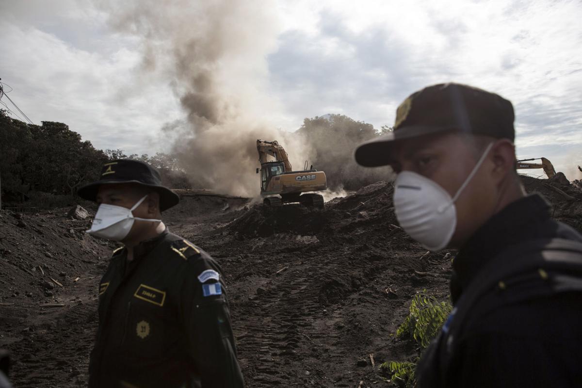 Esta fotografía muestra a dos elementos de la policía mientras una excavadora retira pilas de ceniza volcánica en la localidad de El Rodeo, en Guatemala, el miércoles 6 de junio de 2018. (AP Foto/Rodrigo Abd)