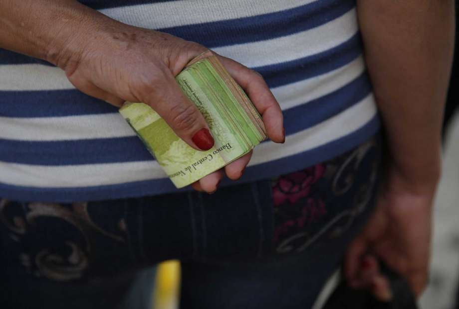 Archivo - En esta foto de archivo del 7 de febrero de 2018, una mujer sostiene un fajo de billetes para pagar el autobús en Caracas, Venezuela. El FMI estimó que la inflación en el país podría alcanzar un millón por ciento en 2018. (AP Foto/Ariana Cubillos, Archivo)