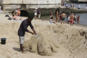 Un hombre rocía agua a su escultura de arena en la orilla del río Tagus en Lisboa, el jueves 2 de agosto de 2018. (AP Foto/Armando Franca)